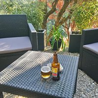 Bottle and glass of beer on a table outside, also showing two outdoor armchairs